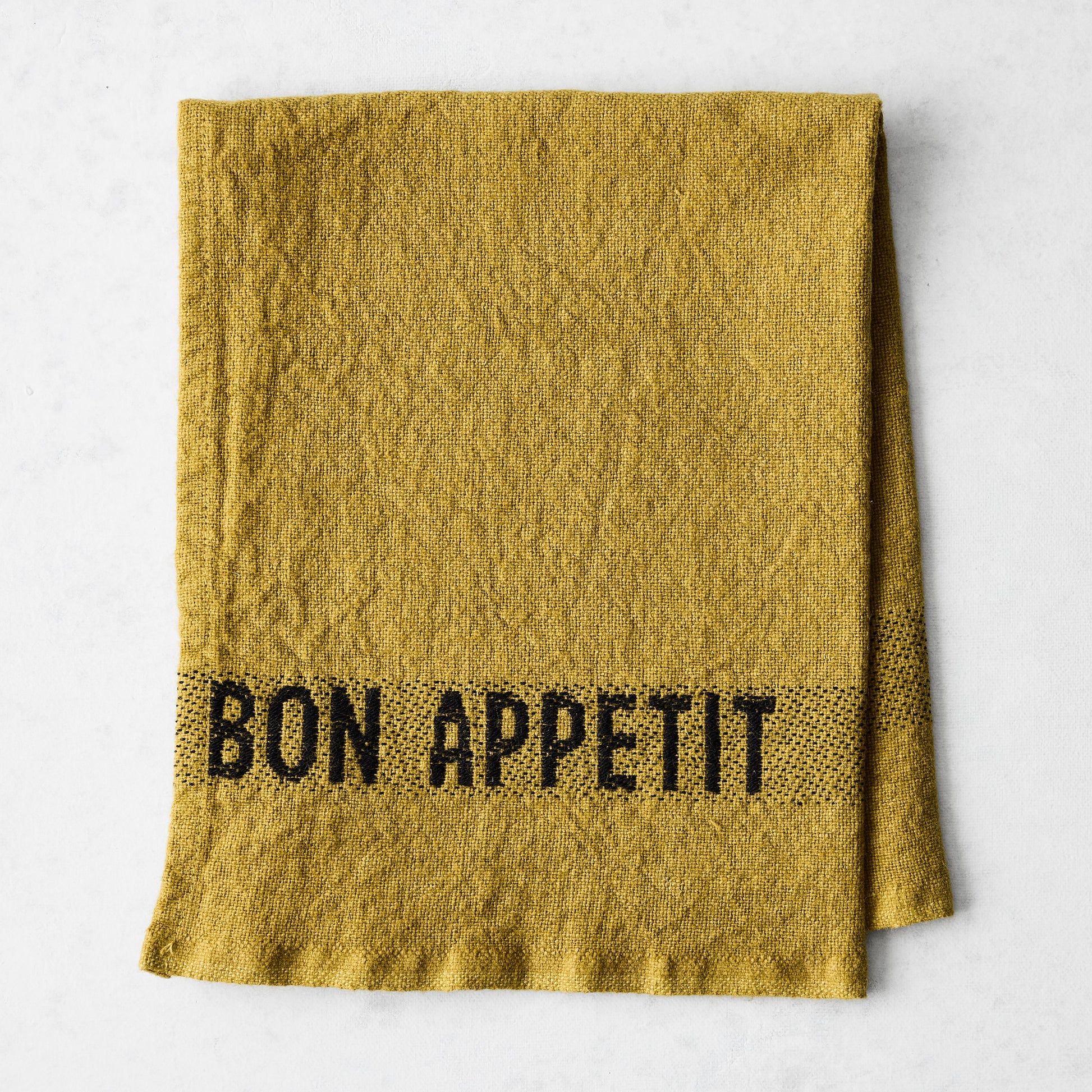 Goldenrod linen napkin with "BON APPETIT" in black lettering, folded on a white surface.