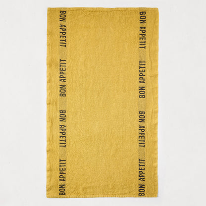 Goldenrod yellow linen hand towel with "Bon Appetit" in black lettering along both long edges.