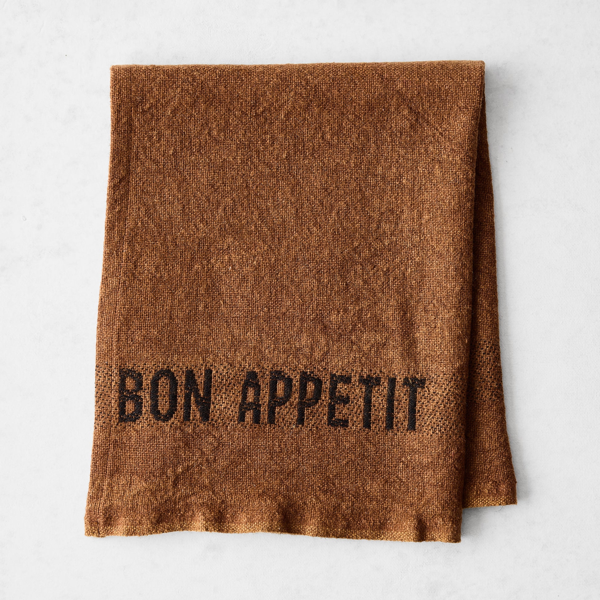 Folded Havane Brown linen napkin with "BON APPETIT" in black lettering.