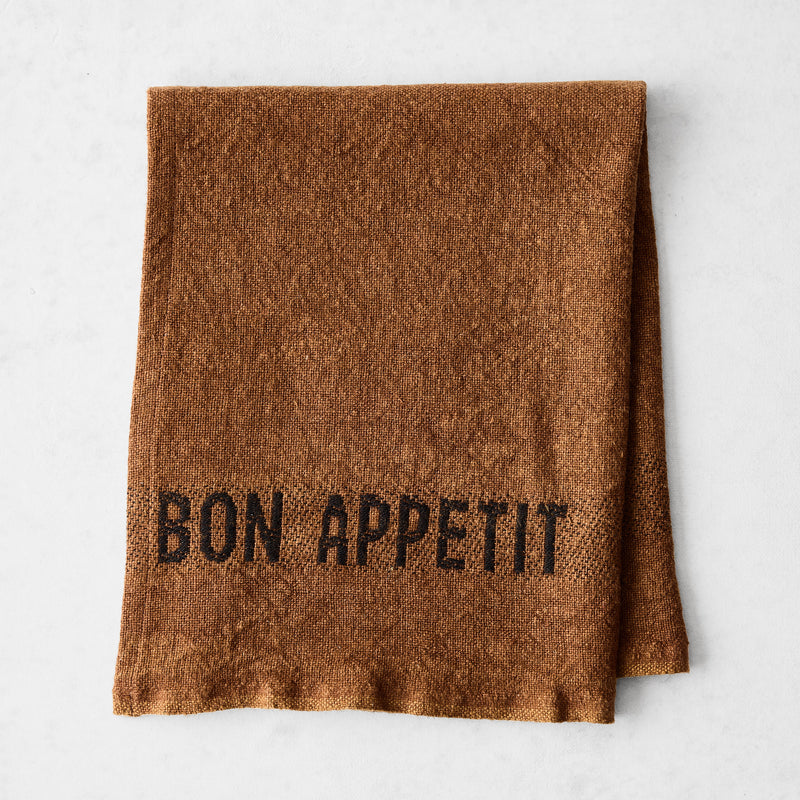Folded Havane Brown linen napkin with "BON APPETIT" in black lettering.