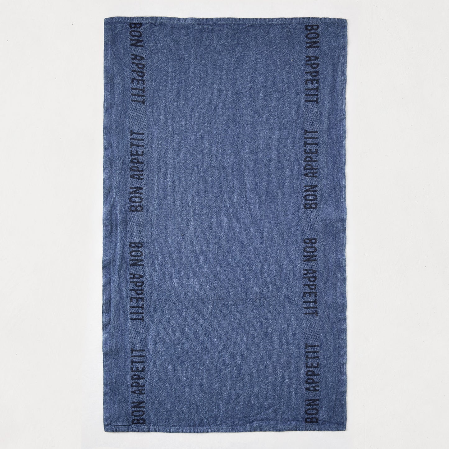 Indigo blue linen hand towel with "Bon Appetit" text in black, laid flat.