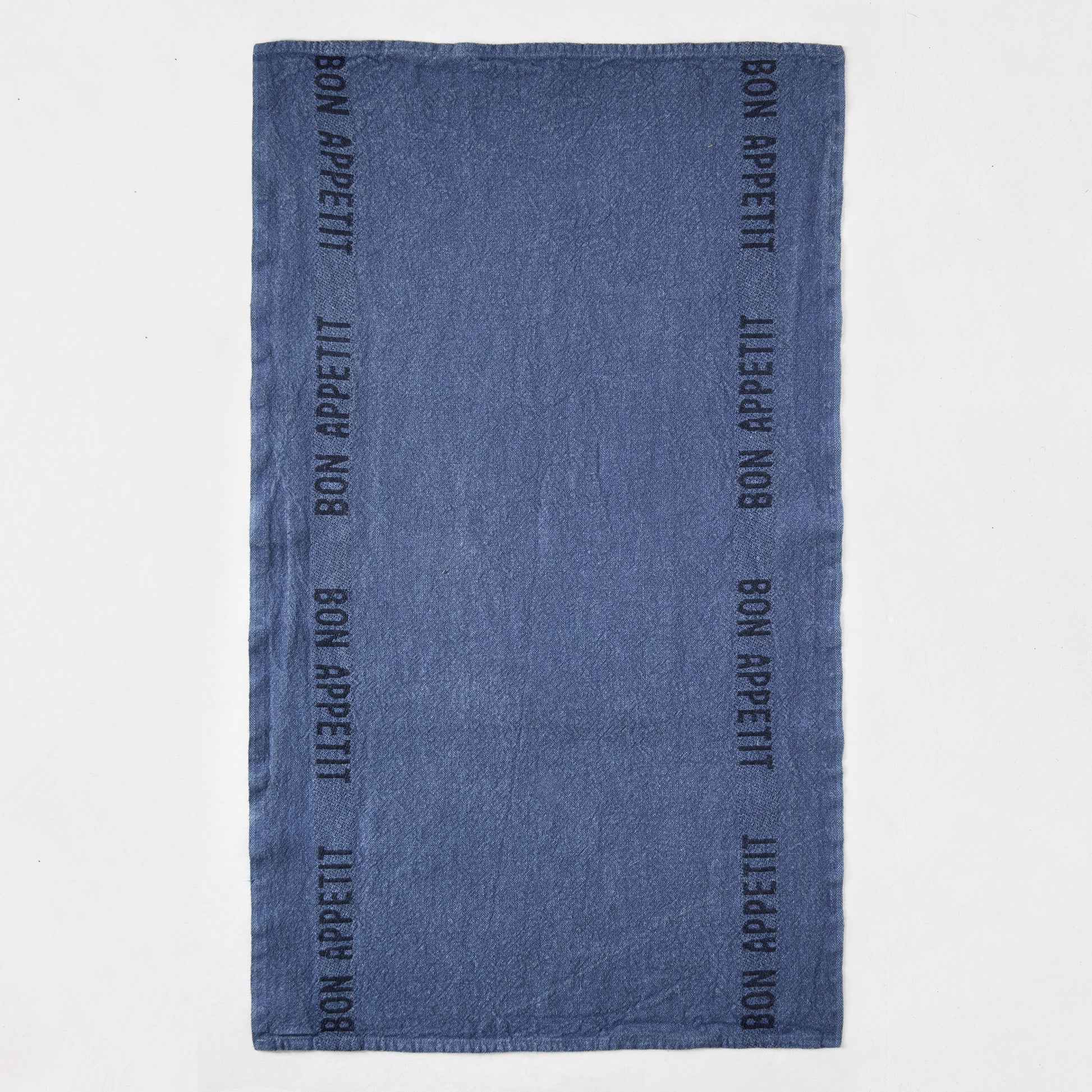 Indigo blue linen hand towel with "Bon Appetit" text in black, laid flat.