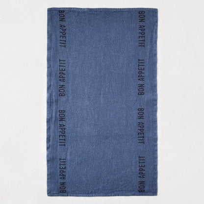Indigo blue linen hand towel with "Bon Appetit" text in black, laid flat.