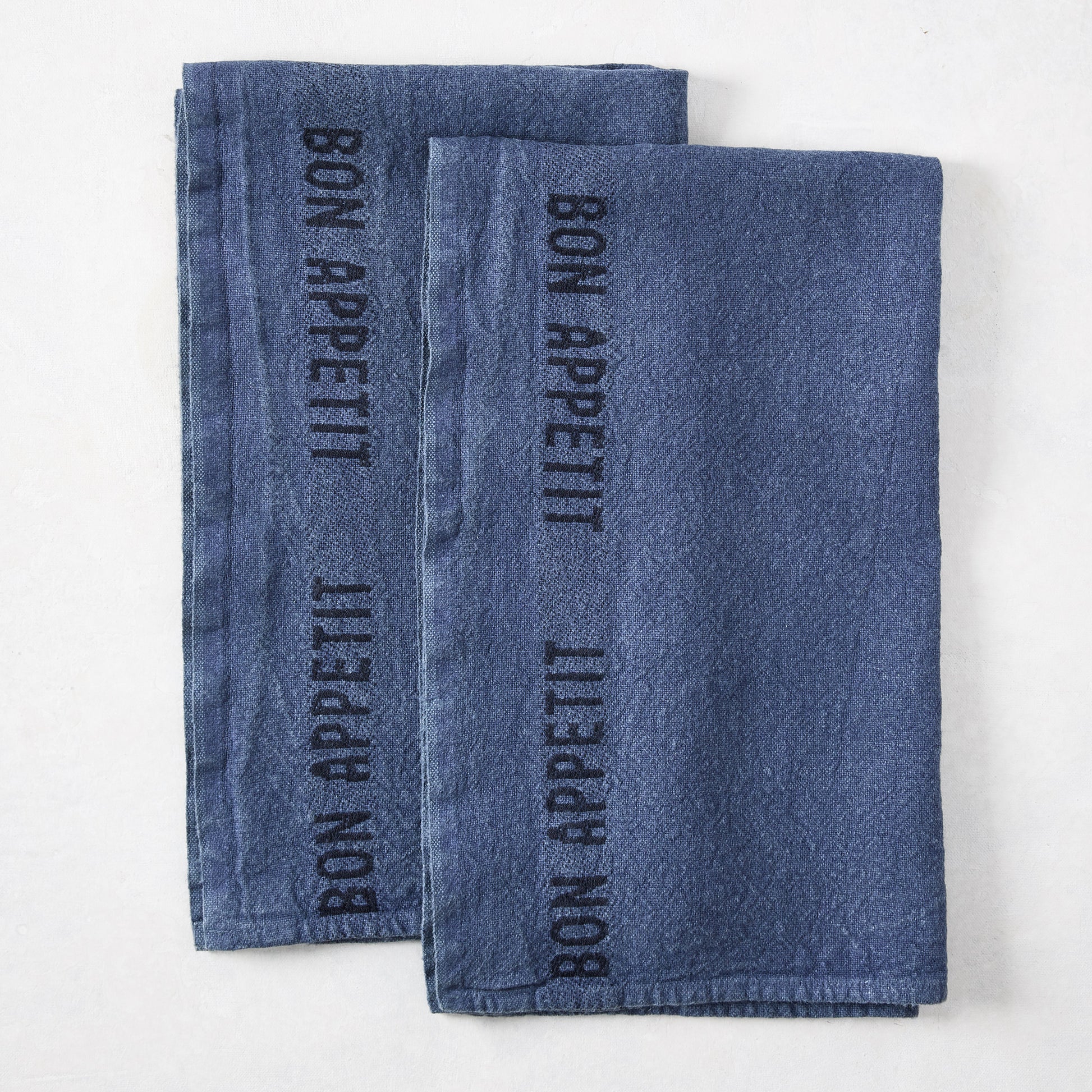 Set of 2 indigo blue linen hand towels with "BON APPETIT" in black lettering.