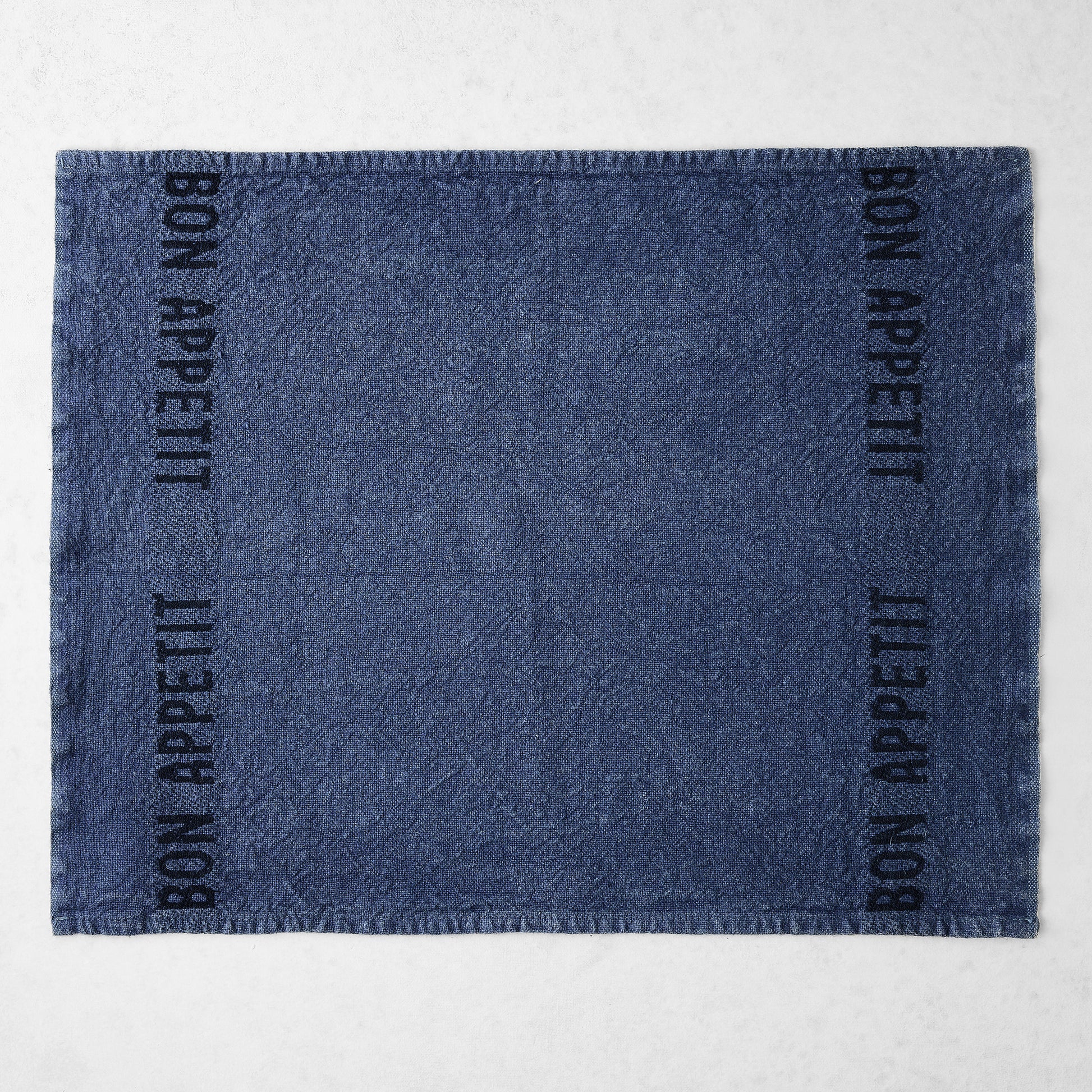 Indigo blue linen napkin with "BON APPETIT" in black lettering on two sides.