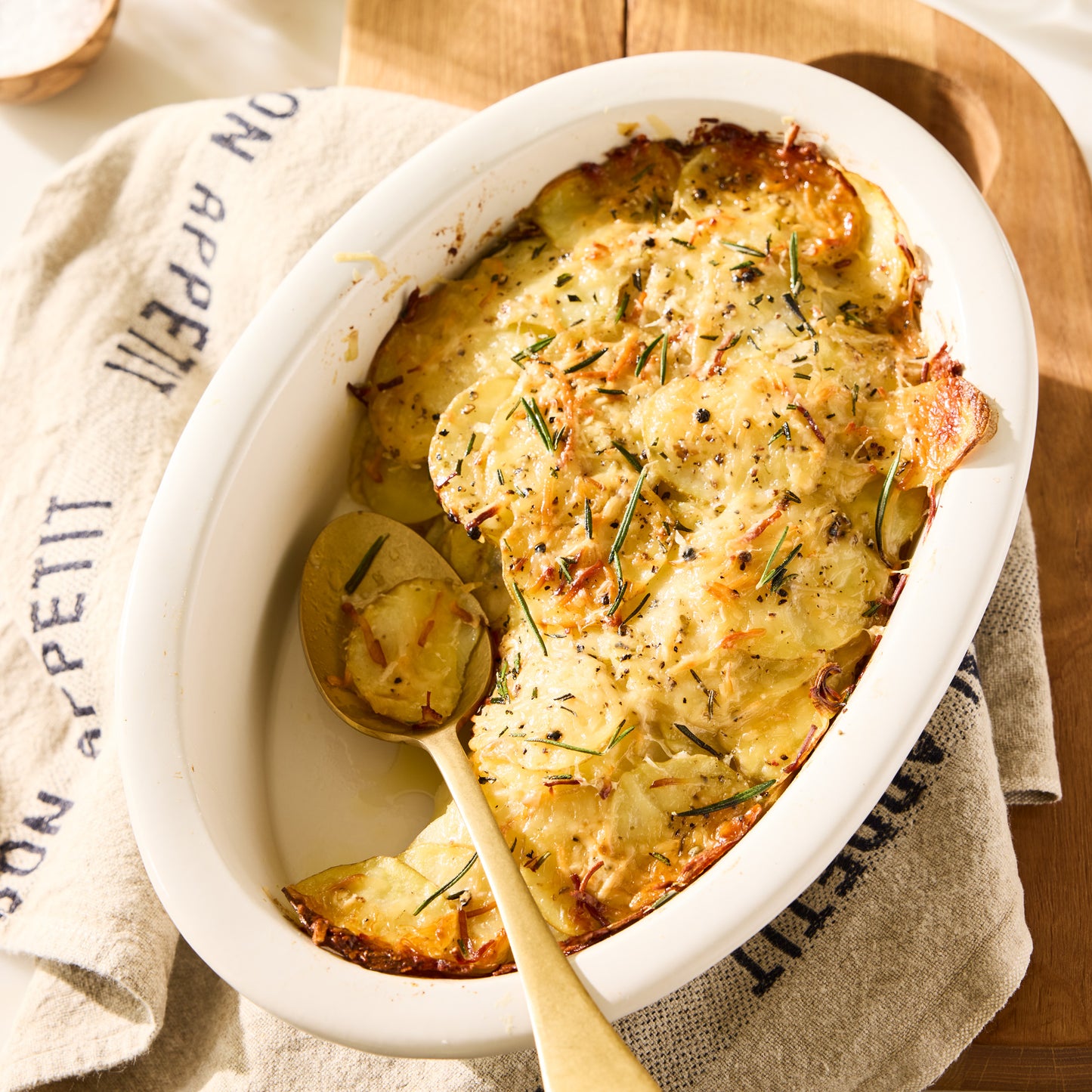 Khaki linen hand towel with "Bon Appetit" in black lettering, draped next to a potato gratin.
