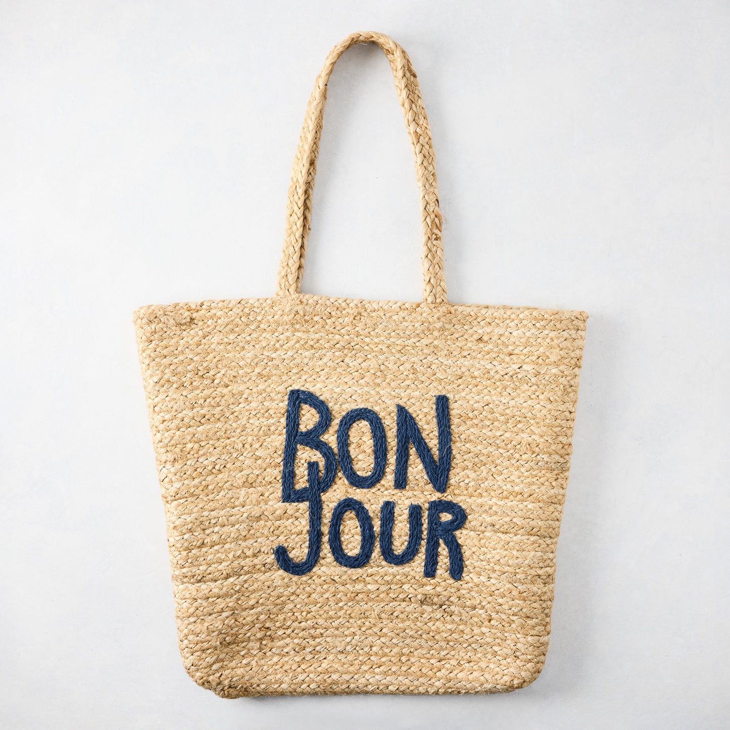 Natural jute woven tote bag with "BON JOUR" embroidered in navy blue.