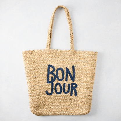 Natural jute woven tote bag with "BON JOUR" embroidered in navy blue.