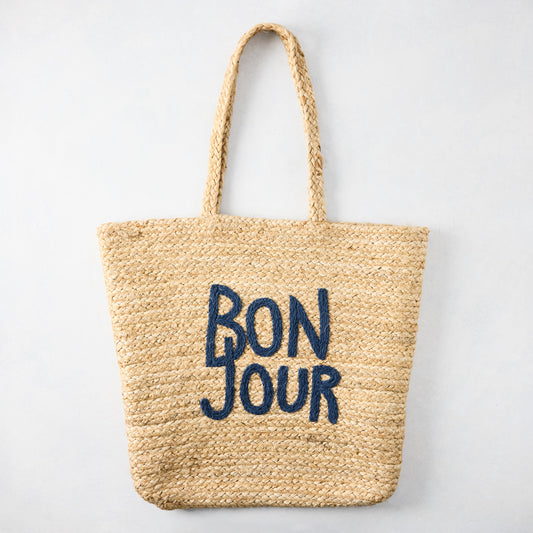 Natural jute woven tote bag with "BON JOUR" embroidered in navy blue.