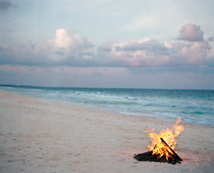 Matt Albiani's "Bonfire" photograph: a beach bonfire with ocean and cloudy sky at dusk.