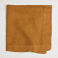 Brass HG Signature hand-dyed linen napkin, 22-inch square, folded, warm golden amber with honey undertones.