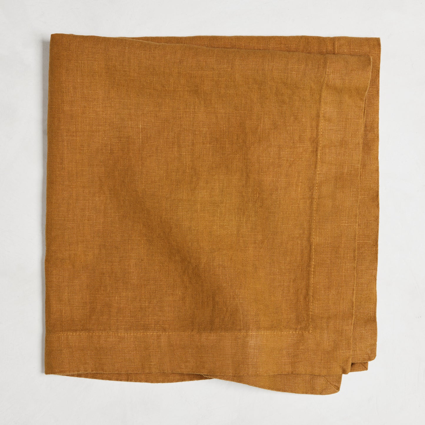 Brass HG Signature hand-dyed linen napkin, 22-inch square, folded, warm golden amber with honey undertones.