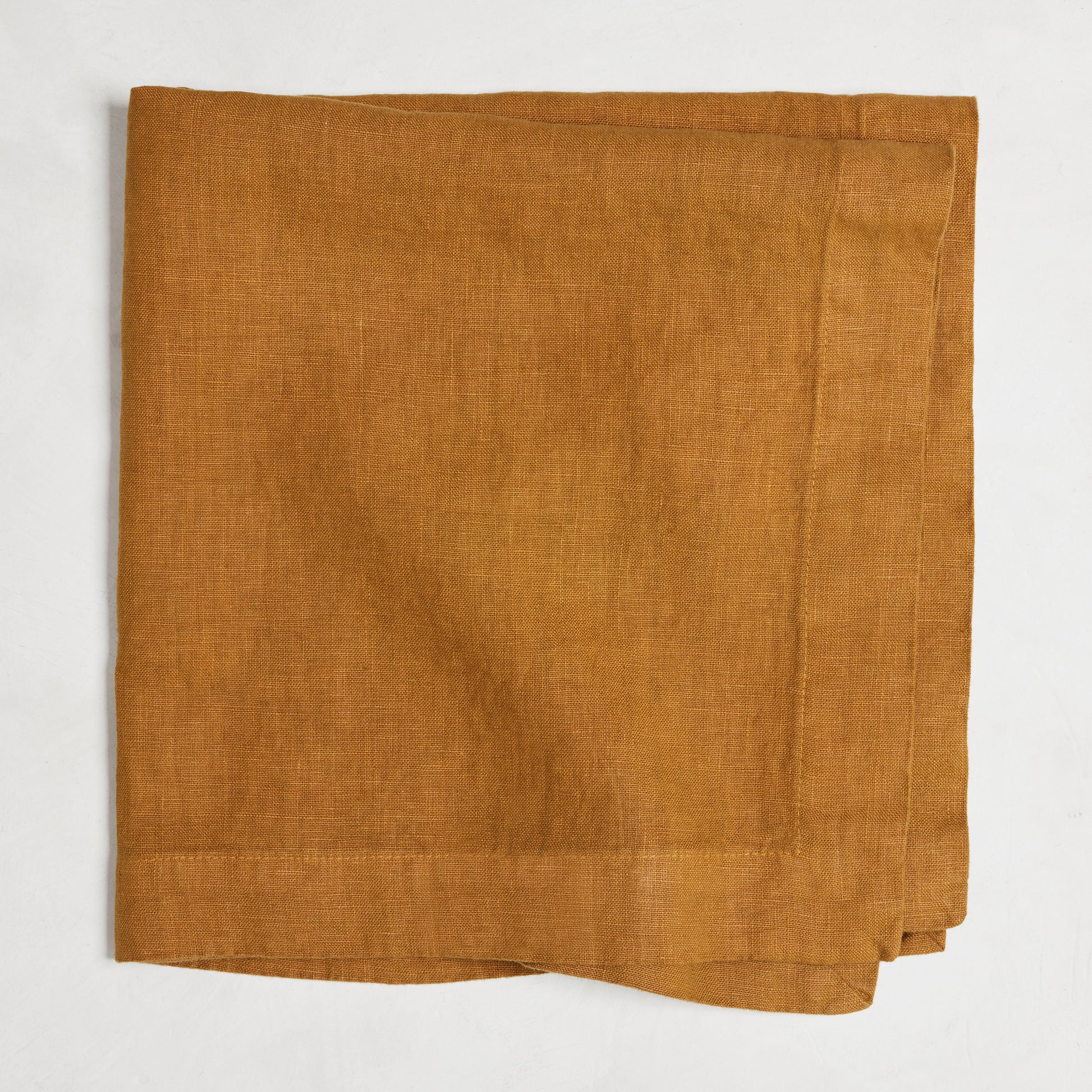 Brass HG Signature hand-dyed linen napkin, 22-inch square, folded, warm golden amber with honey undertones.