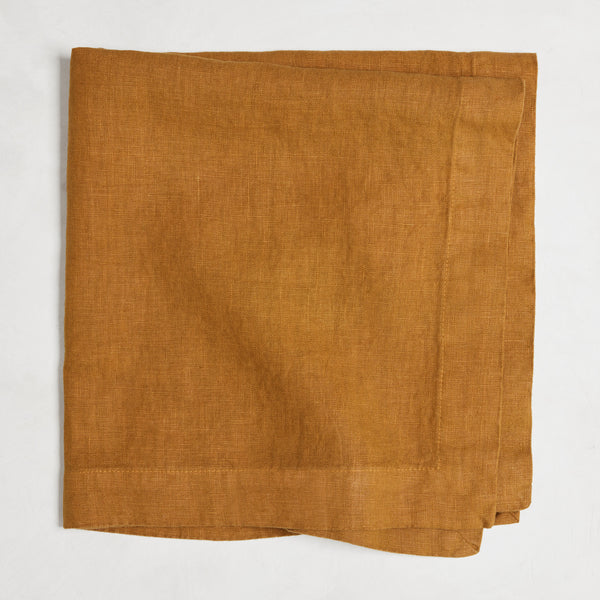 Brass HG Signature hand-dyed linen napkin, 22-inch square, folded, warm golden amber with honey undertones.