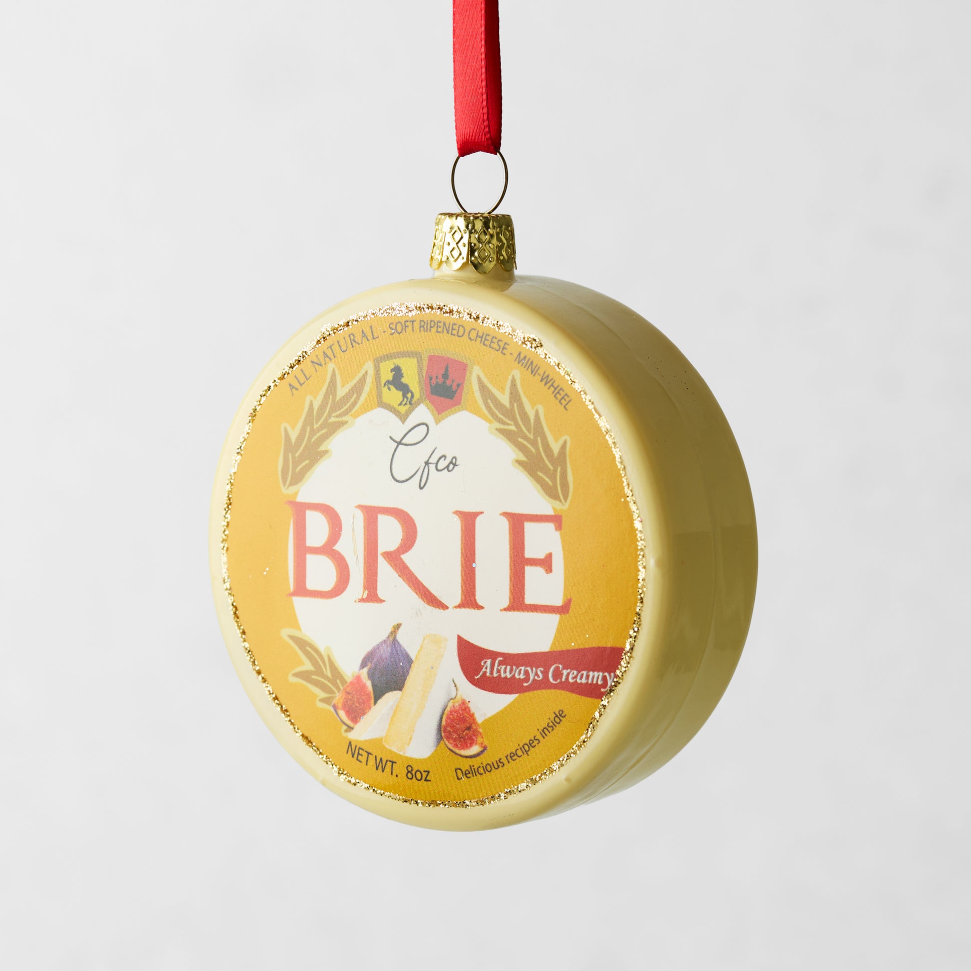 Round glass Brie cheese Christmas ornament with gold glitter and red ribbon.