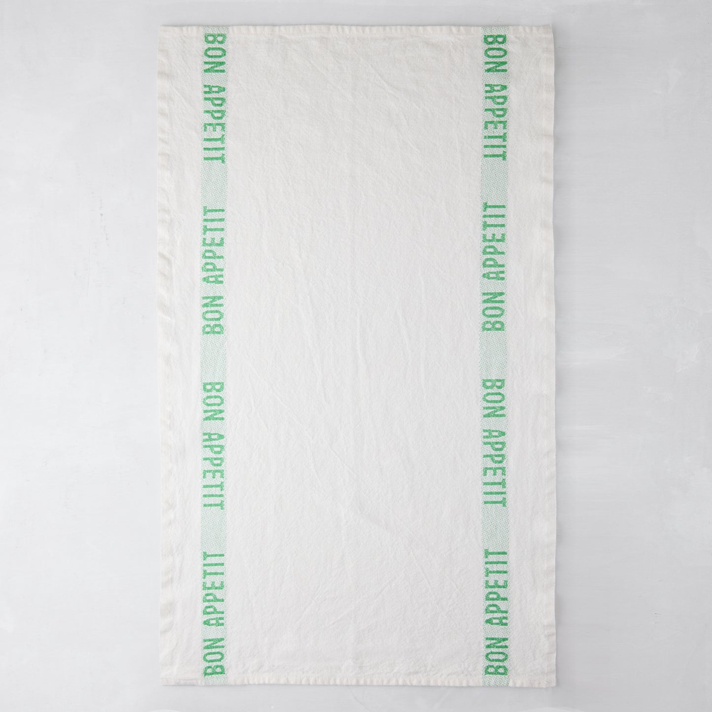 White linen hand towel with vertical bright green "Bon Appetit" text stripes on each side.