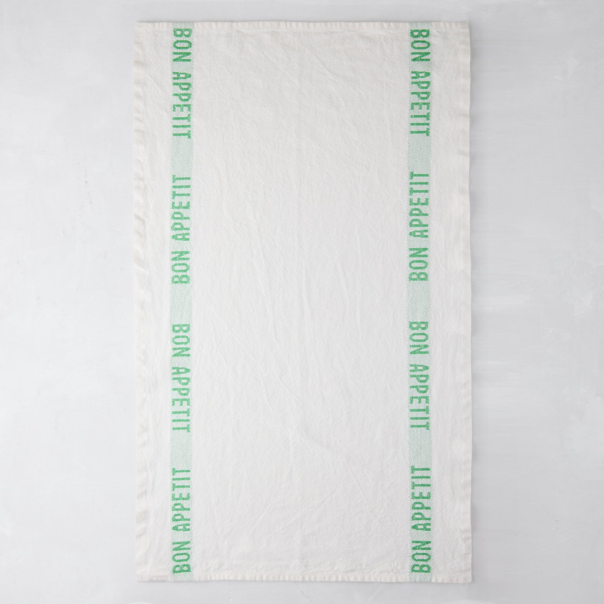 White linen hand towel with vertical bright green "Bon Appetit" text stripes on each side.