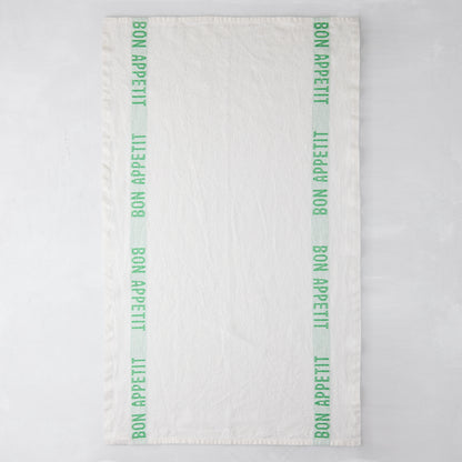 White linen hand towel with vertical bright green "Bon Appetit" text stripes on each side.