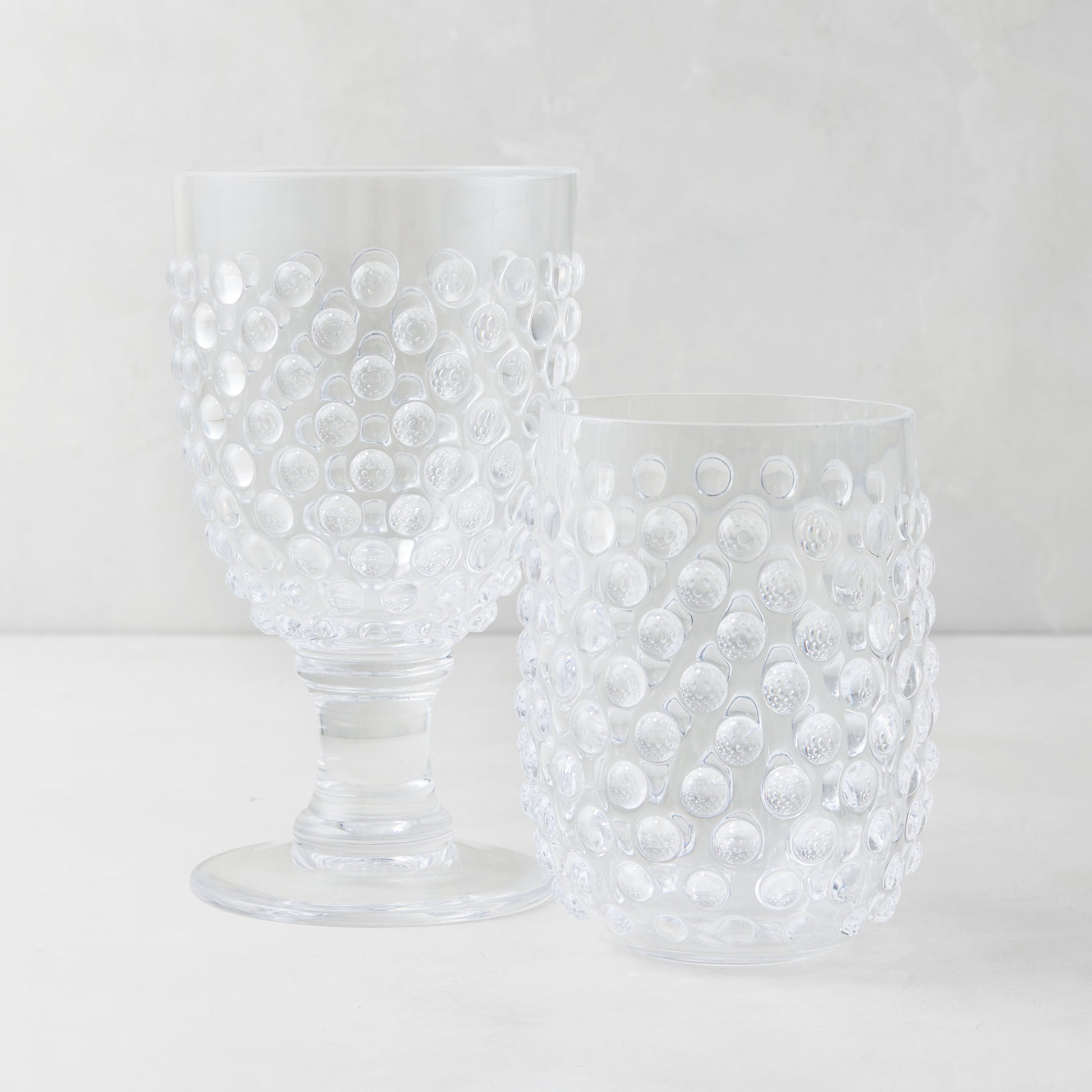 Clear acrylic bubble wine glass and tumbler with textured hobnail design.