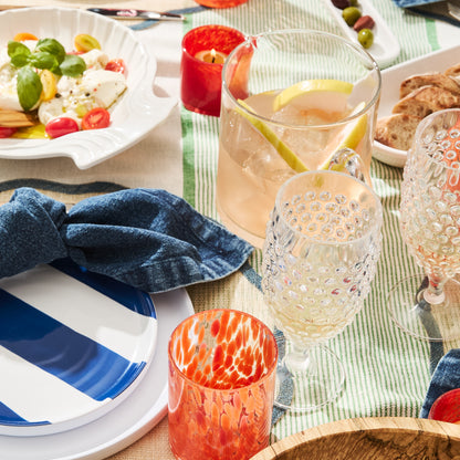 Clear acrylic bubble wine glass on a striped tablecloth with other outdoor dining items.