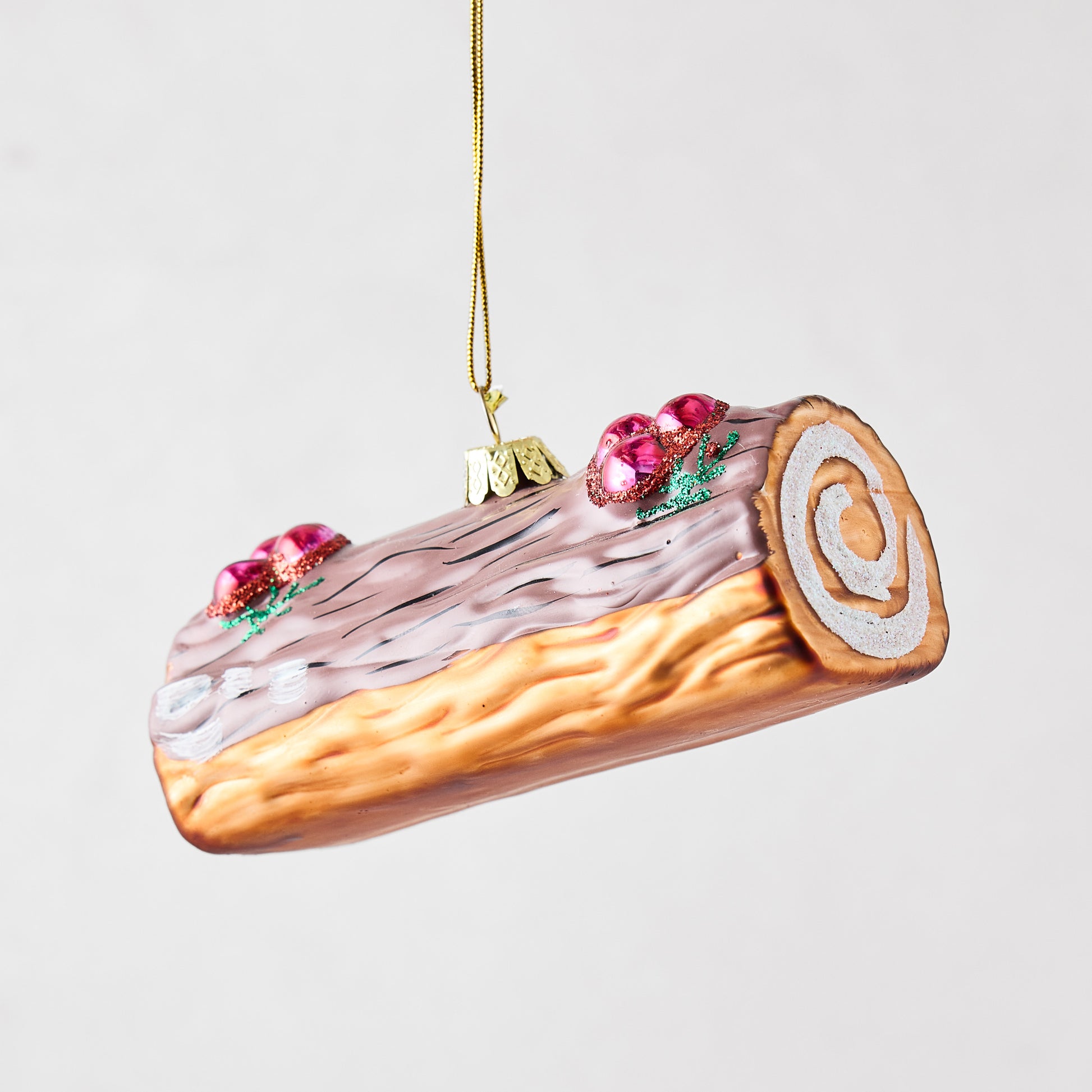 Hand-painted glass Buche de Noel Christmas ornament with pink icing, glittered berries, and a golden hanging string.