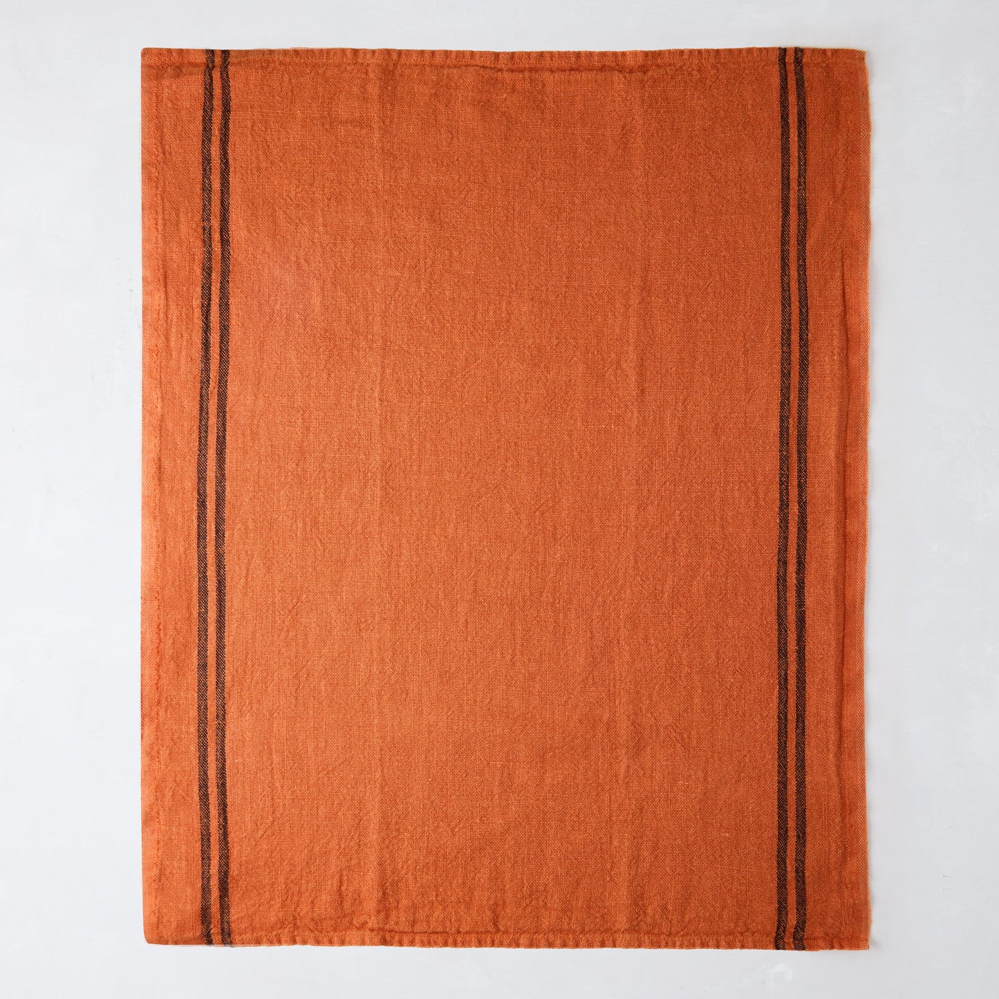 Burnt orange French linen towel with two dark brown stripes along the left edge.