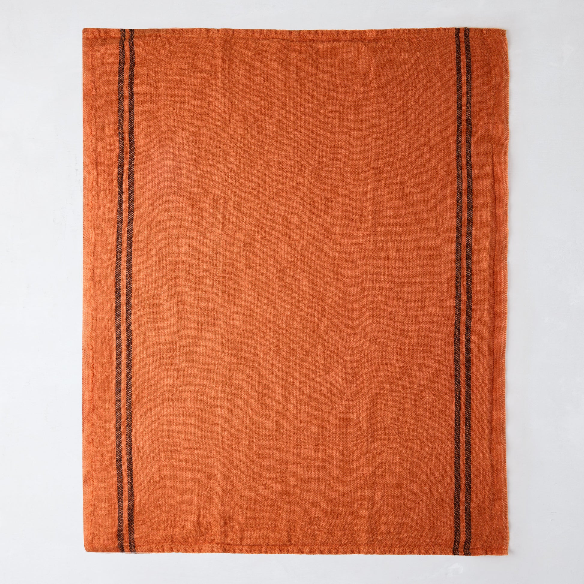 Burnt orange French linen towel with two dark brown stripes along the left edge.