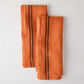Set of 2 burnt orange French linen towels with dark brown stripes, folded on a white surface.