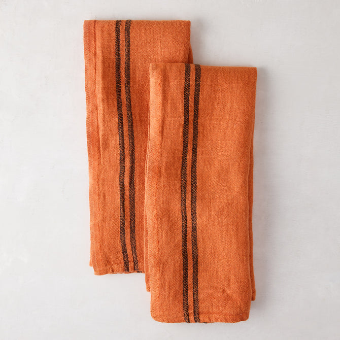 Set of 2 burnt orange French linen towels with dark brown stripes, folded on a white surface.