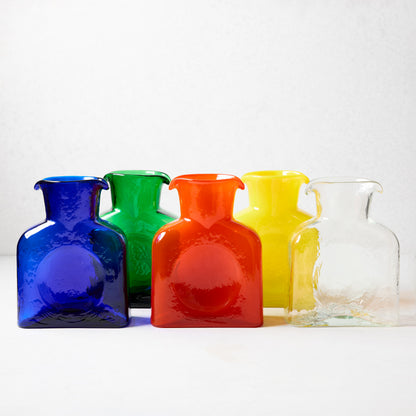 Five square glass pitchers: blue, green, red, yellow, and clear, with dual spouts.