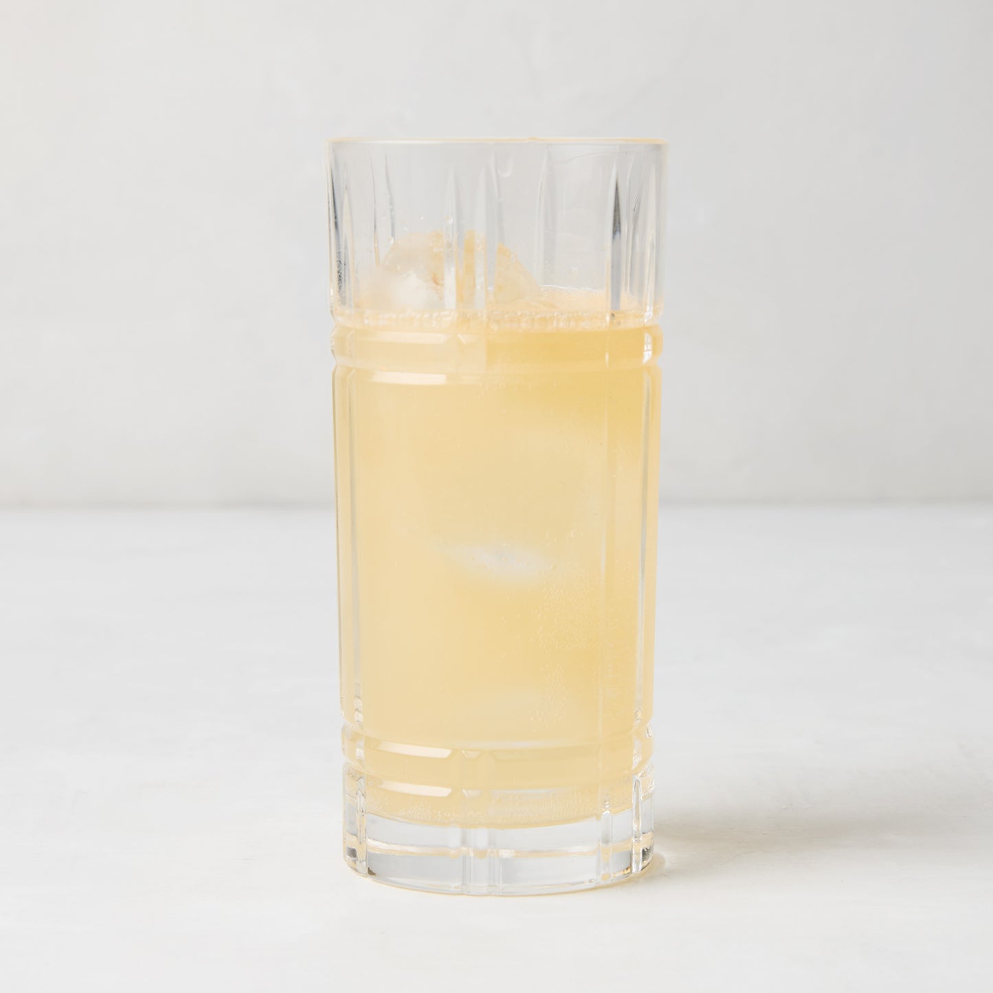 Camden Eco-Crystal High Ball Glass, clear, sleek, slender, filled with a light yellow drink and ice.
