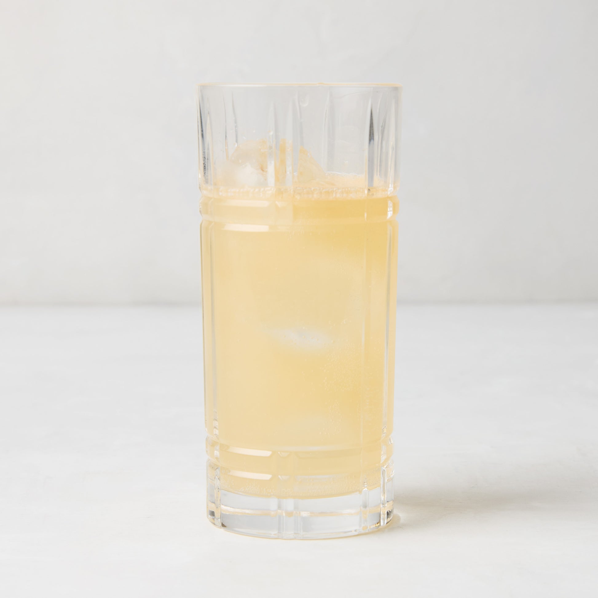 Camden Eco-Crystal High Ball Glass, clear, sleek, slender, filled with a light yellow drink and ice.