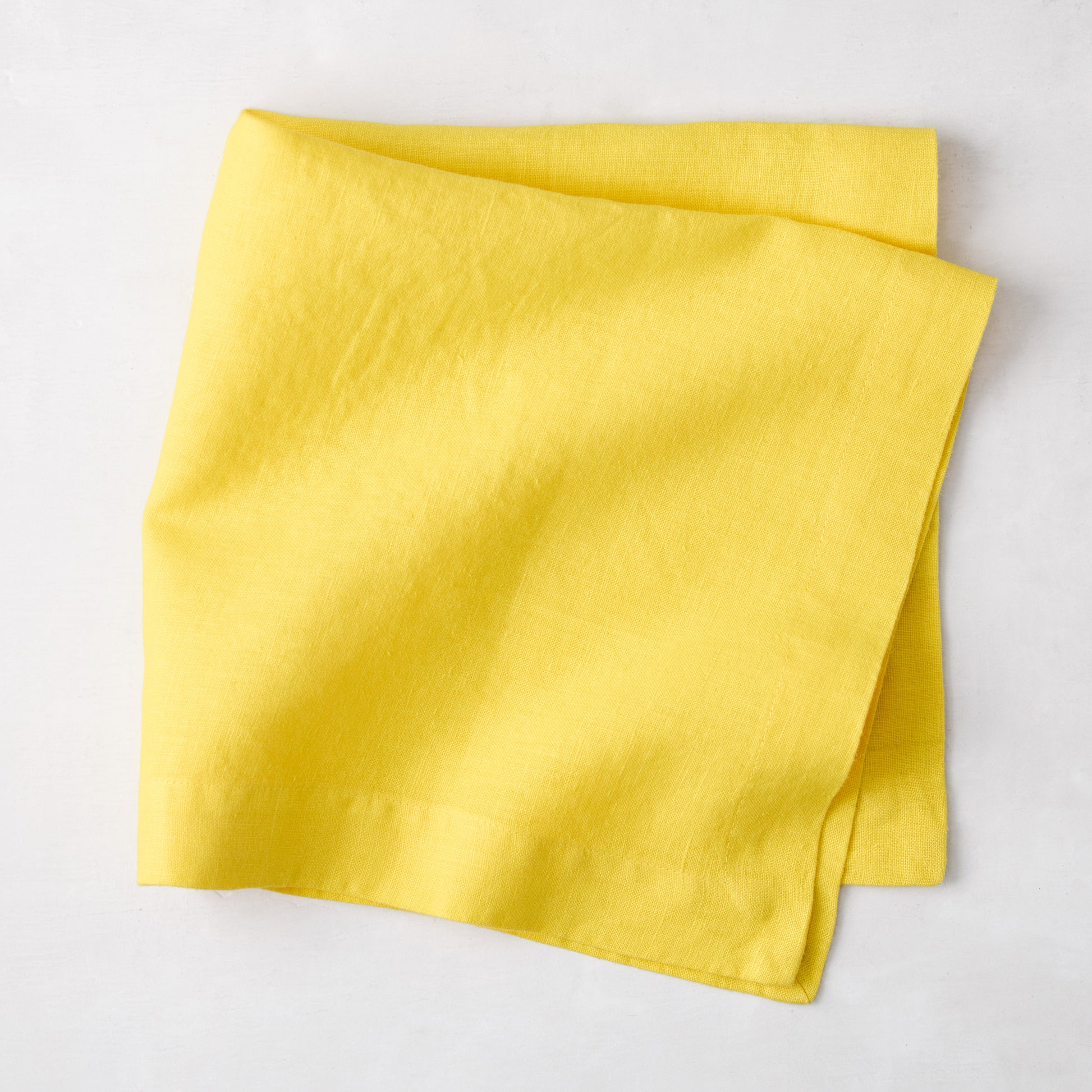 Canary HG Signature Hand-Dyed Linen Napkin, bright buttery yellow, folded on a white surface.