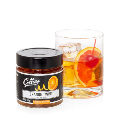 Collins Orange Twist in Syrup cocktail garnish jar next to a whiskey cocktail with orange slice and cherry.