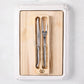 Jean Dubost stainless steel carving knife and fork set on a removable oak wood insert inside a white ceramic cutting board.