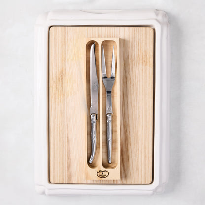 Jean Dubost stainless steel carving knife and fork set on a removable oak wood insert inside a white ceramic cutting board.