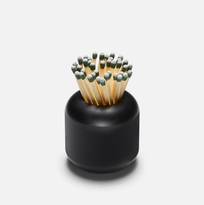 Black cast iron match striker with deep knurling, filled with green-tipped matches.