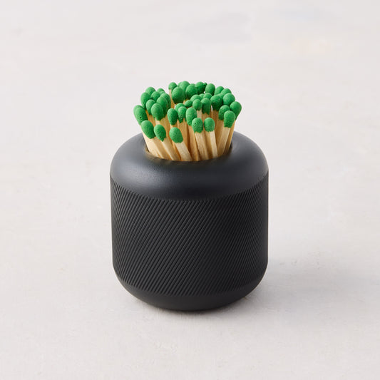 Black cast iron match striker with deep knurling, holding matches with green tips.