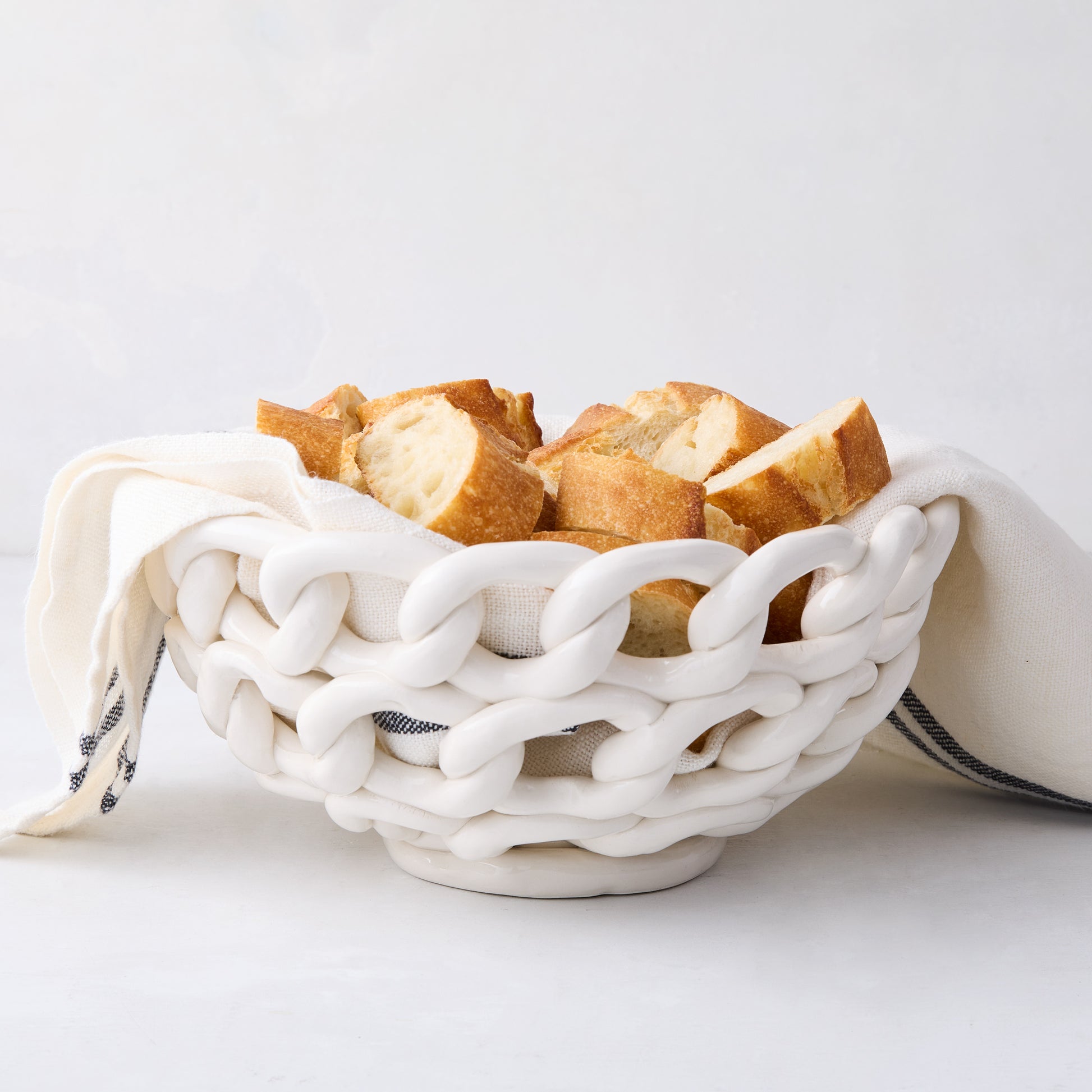 White ceramic woven bread bowl with sliced baguette and a linen napkin.