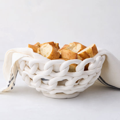 White ceramic woven bread bowl with sliced baguette and a linen napkin.