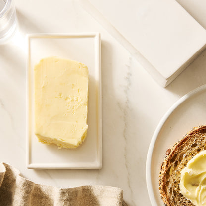 White ceramic butter dish with a stick of European butter, next to toast and a linen napkin.