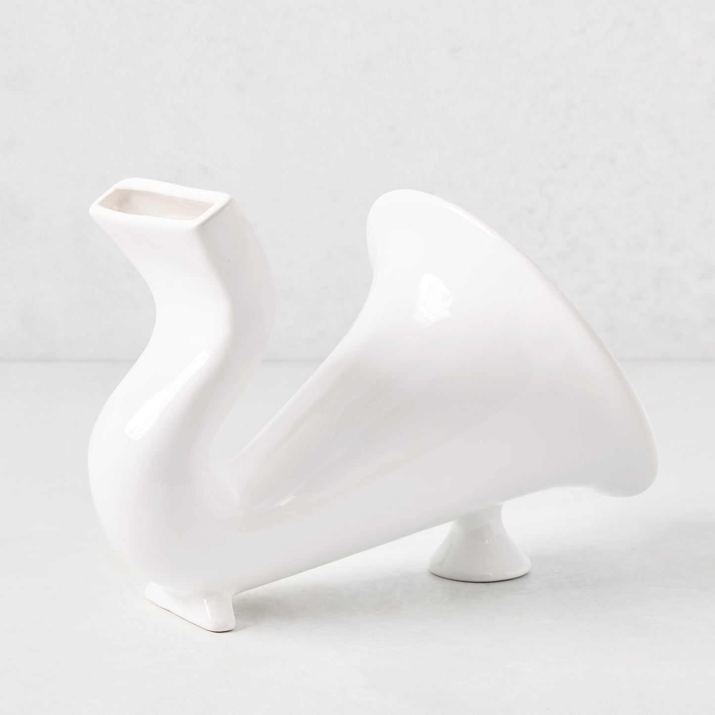 White ceramic speaker with a curved, horn-like design and rectangular phone slot.