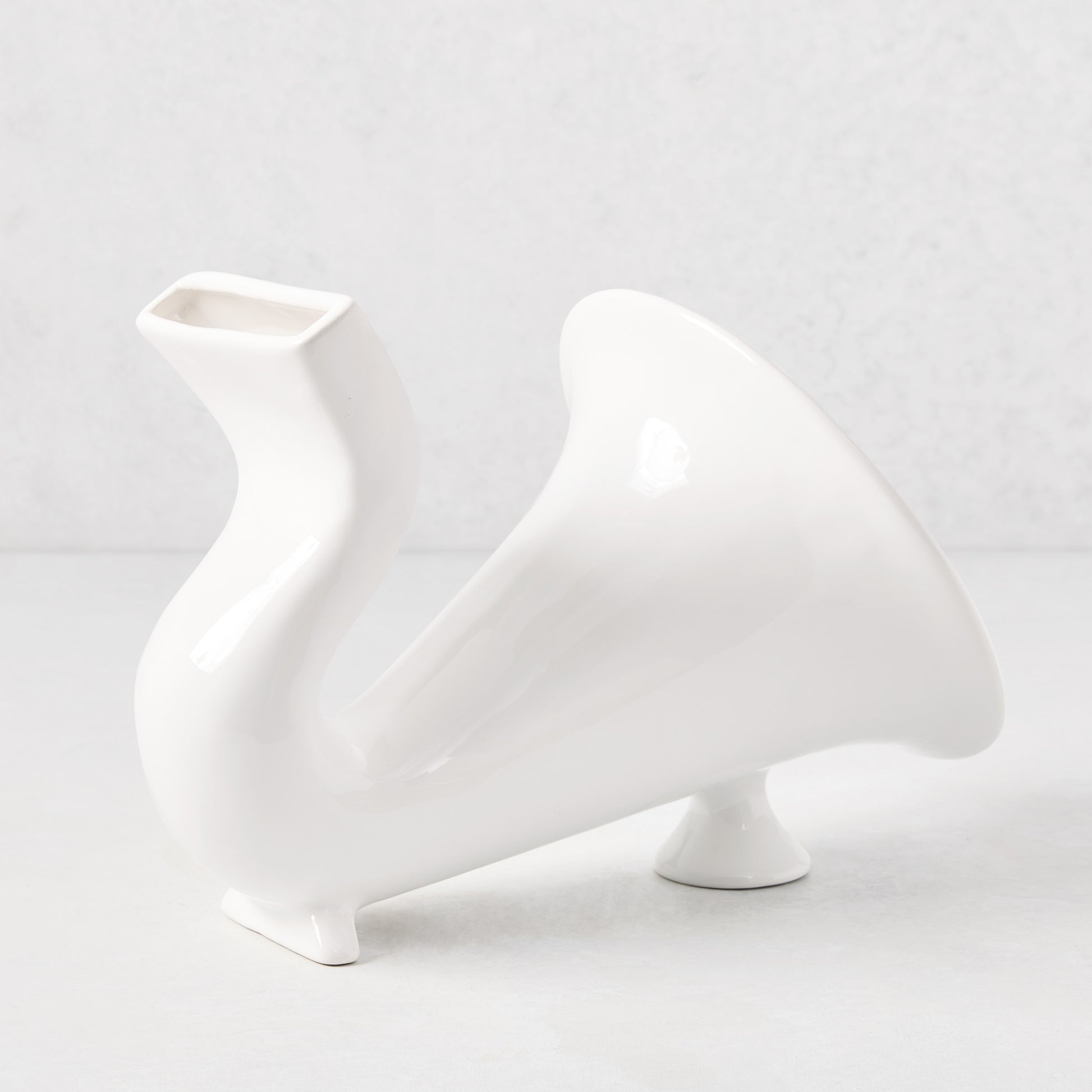 White ceramic speaker with a curved, horn-like design and rectangular phone slot.