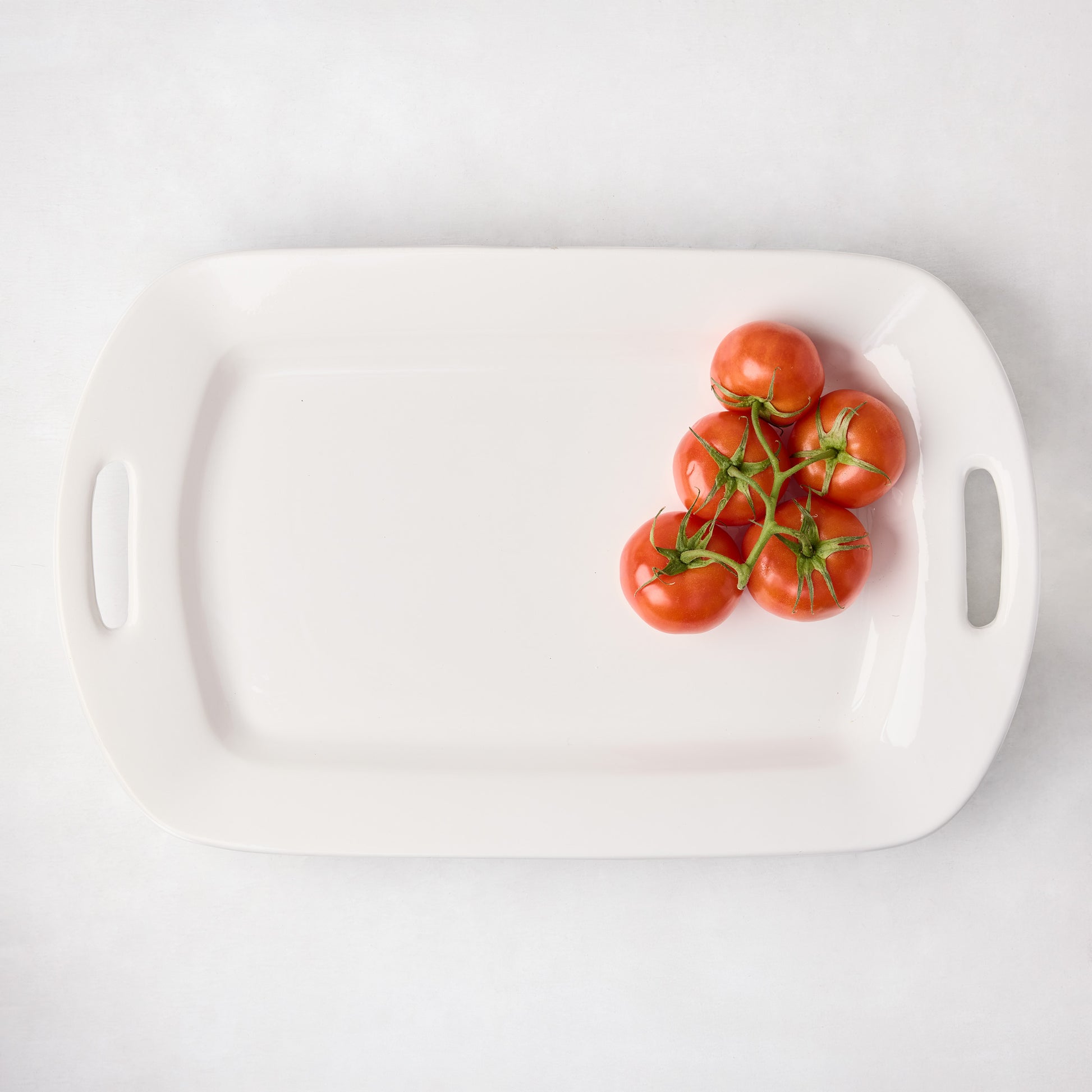 White ceramic handled serving platter with five red tomatoes on the right.