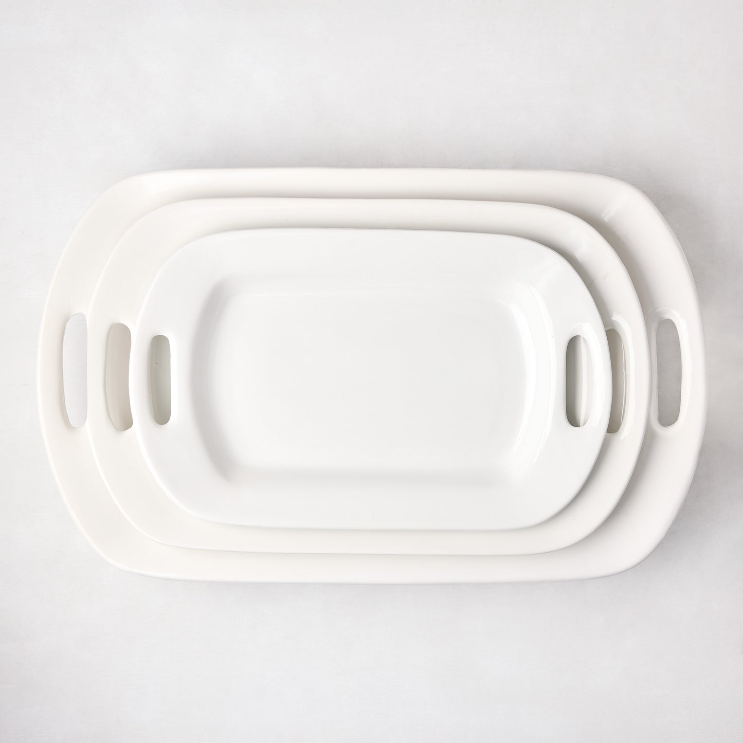 Three nested white ceramic serving platters with handles, largest 13"W x 21"L.