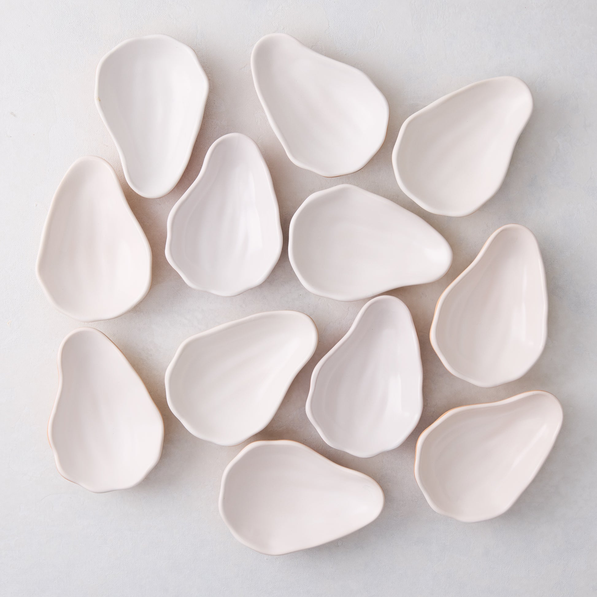 Set of 12 handmade ceramic oyster shells in a natural, light cream color, scattered on a white surface.
