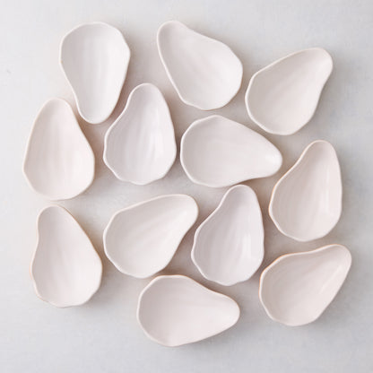 Set of 12 handmade ceramic oyster shells in a natural, light cream color, scattered on a white surface.
