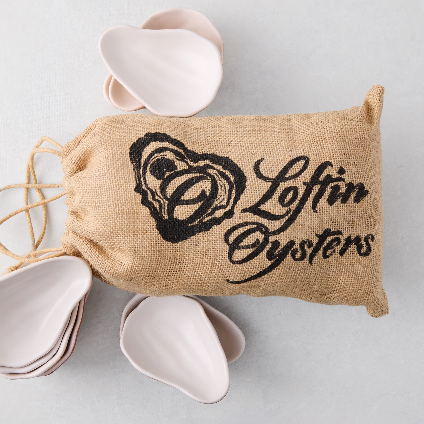 Ceramic oyster shells, light pink, in a burlap bag with "Loftin Oysters" logo.