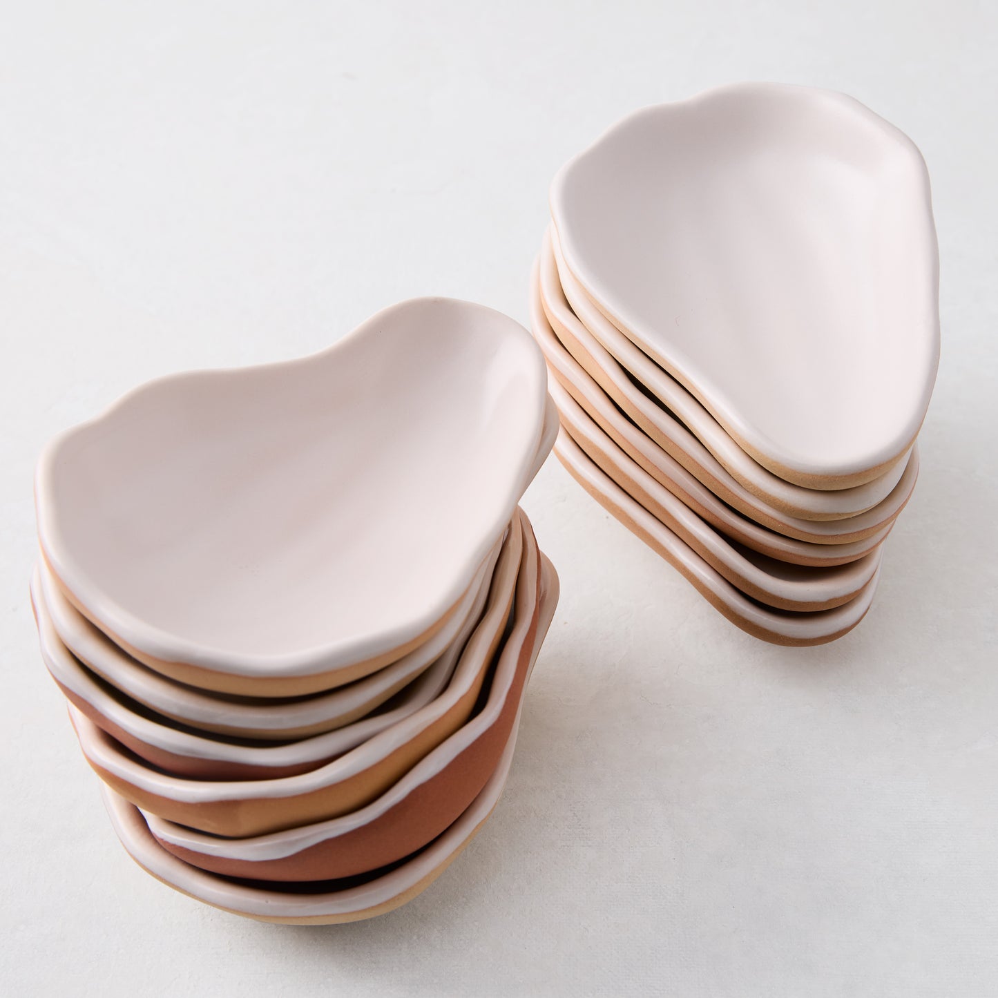 Two stacks of light pink ceramic oyster shells with natural clay undersides on a white surface.