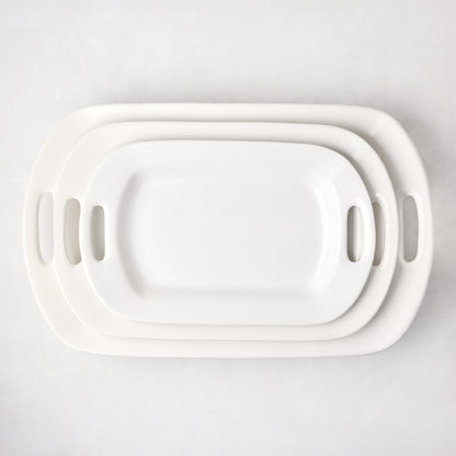 Three nested white ceramic serving platters with handles, varying in size.